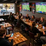 Engaging sports betting moment at 27G, patrons actively using mobile apps while watching live games.